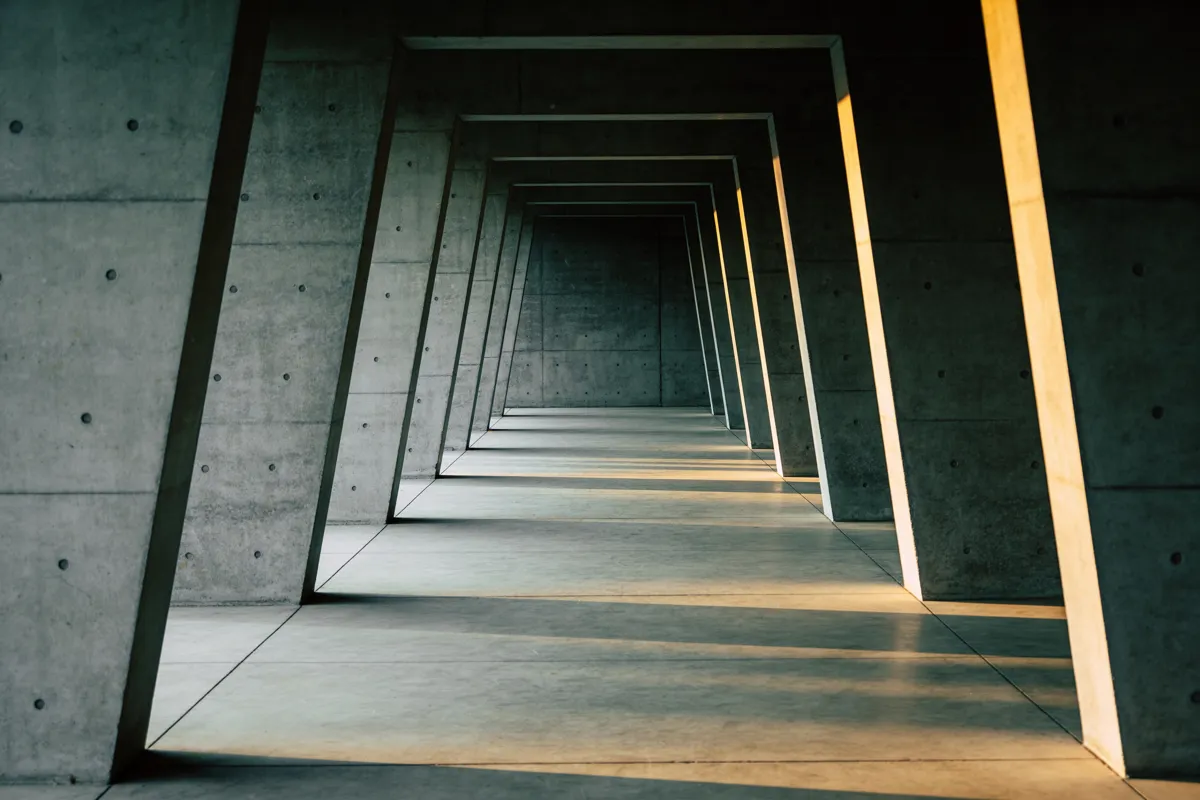 A deep concrete colonnade of repeating structural bays receding into shadow